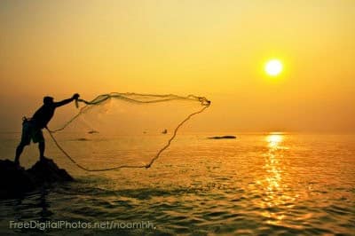 Person casting net into water at sunset.
