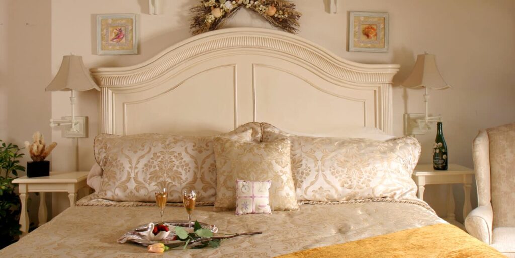 Room showing off-white king headboard with seashore décor and champagne and chocolate covered strawberries.