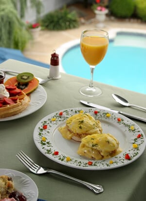 Breakfast plates of eggs, waffles, and fruit by the pool at Sand Castle B&B