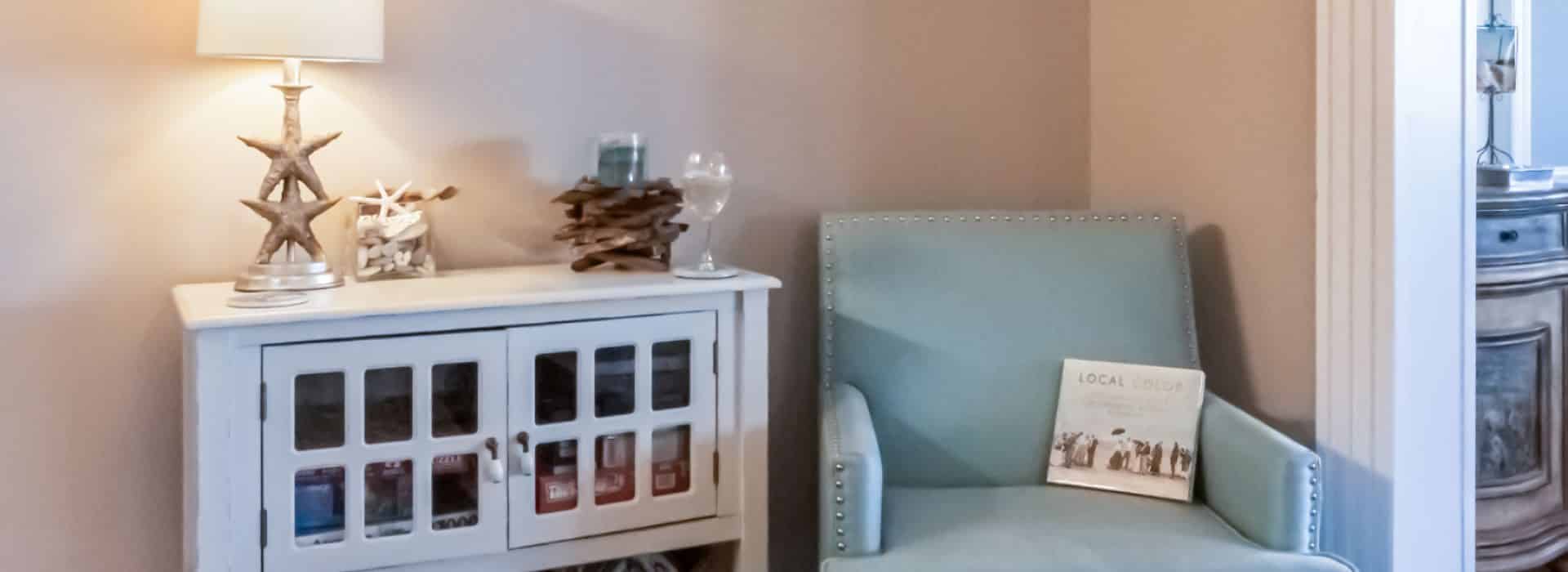 Small nook area with blue upholstered chair next to white cabinet with glass doors