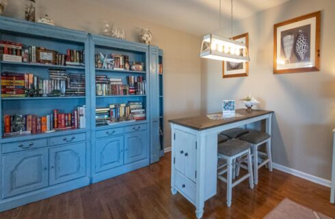 Game room with light tan walls, hardwood flooring, and blue wooden bookcase full of books and games