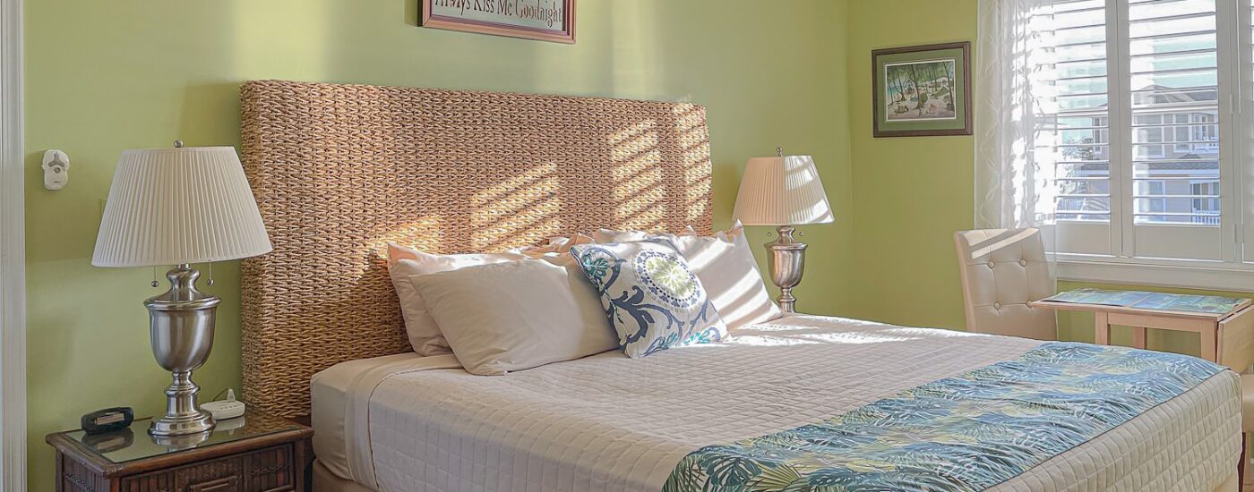 Bedroom with lime green walls, hardwood flooring, wicker bed, white bedding, and dark wooden nightstand