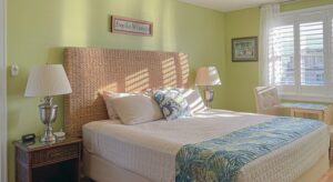 Bedroom with lime green walls, hardwood flooring, wicker bed, white bedding, and dark wooden nightstand