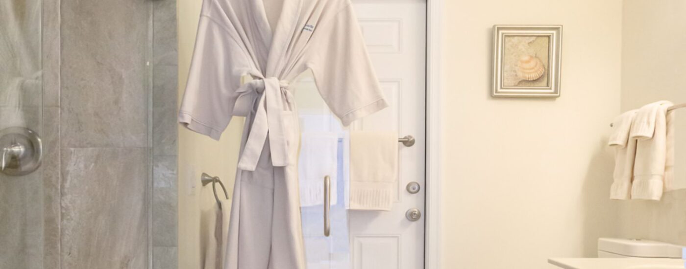 Bathroom with light cream walls, walk in tiled shower, white vanity, white countertop, and a hanging white robe