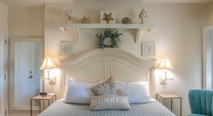 Bedroom with cream walls, cream wood headboard, white and gray bedding, and turquoise upholstered chair