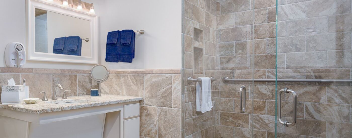 Bathroom with tiled walls, walk in tiled shower, white vanity, and quartz countertop