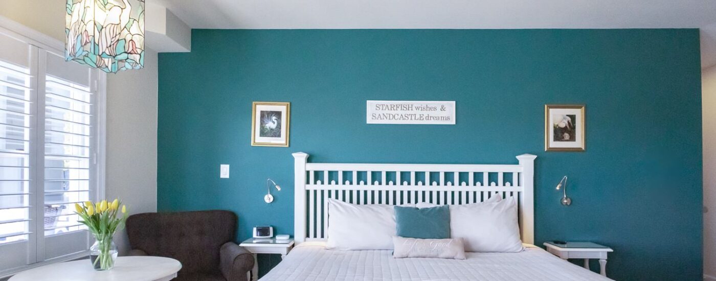 Bedroom with turquoise and off-white walls, white wooden headboard, white bedding, and sitting area