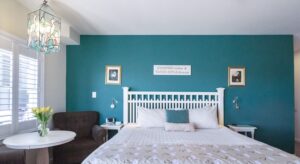 Bedroom with turquoise and off-white walls, white wooden headboard, white bedding, and sitting area