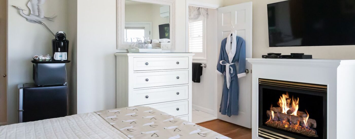 Bedroom with white walls, white bedding, white dresser, and fireplace
