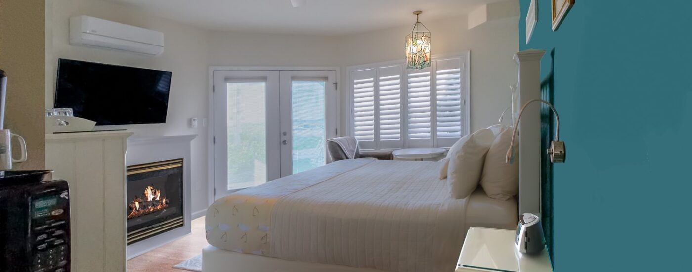 Bedroom with turquoise and white walls, white wooden headboard, white bedding, sitting area, and fireplace