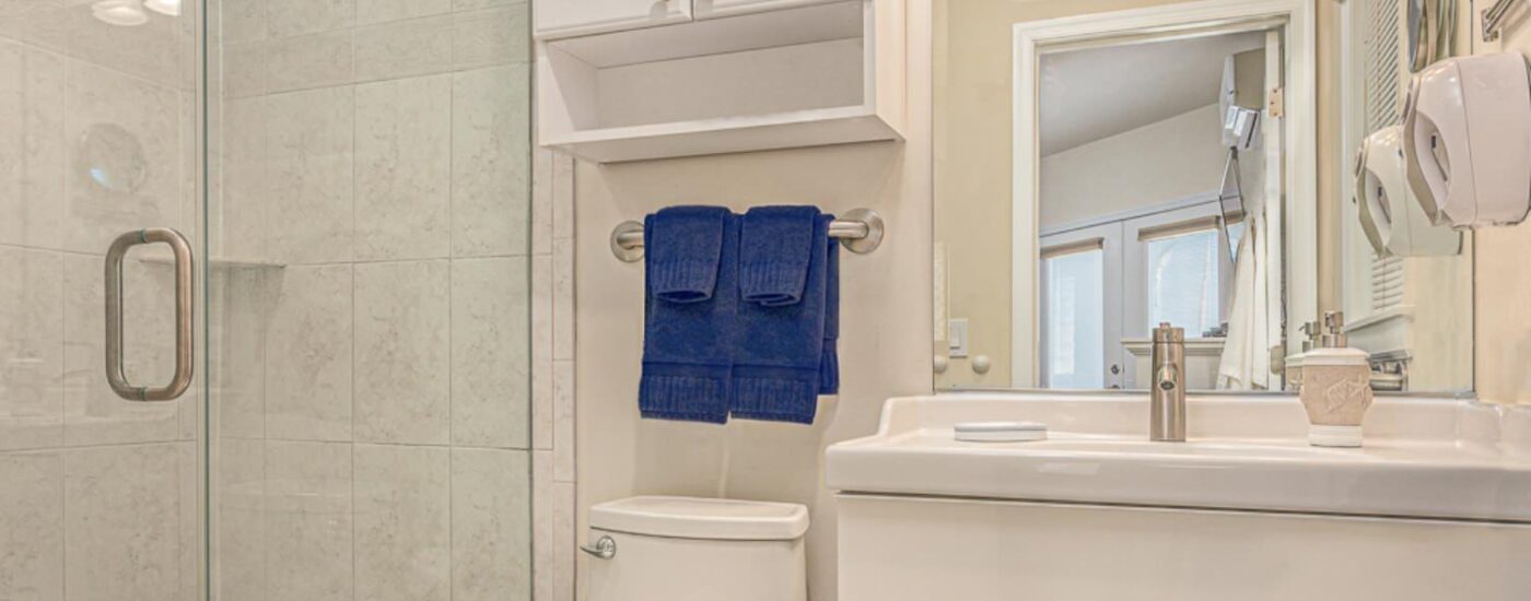 Bathroom with light colored walls, tiled walk-in shower, white sink, and white vanity