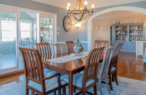 Dining room with light blue walls, hardwood flooring, wood table and chairs, and view into game room