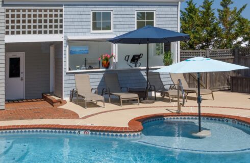 Exterior view of property with light gray shake siding and white trim, patio, pool, and patio furniture