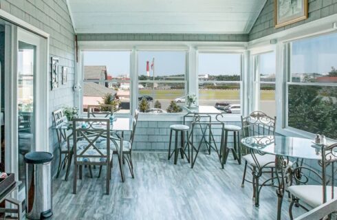 Large breakfast dining area with multiple windows, hardwood flooring, and metal chairs and tables with glass tops