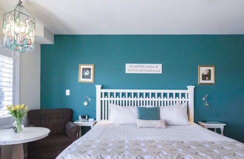 Bedroom with turquoise and off-white walls, white wooden headboard, white bedding, and sitting area