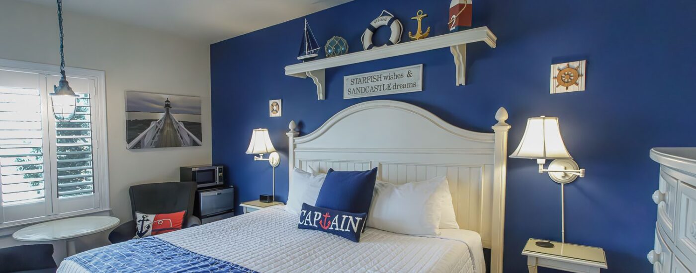 Bedroom with blue and white walls, hardwood flooring, white wood bed, white bedding, and sitting area
