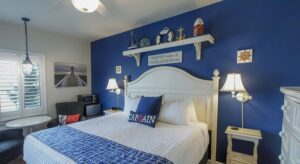 Bedroom with blue and white walls, hardwood flooring, white wood bed, white bedding, and sitting area