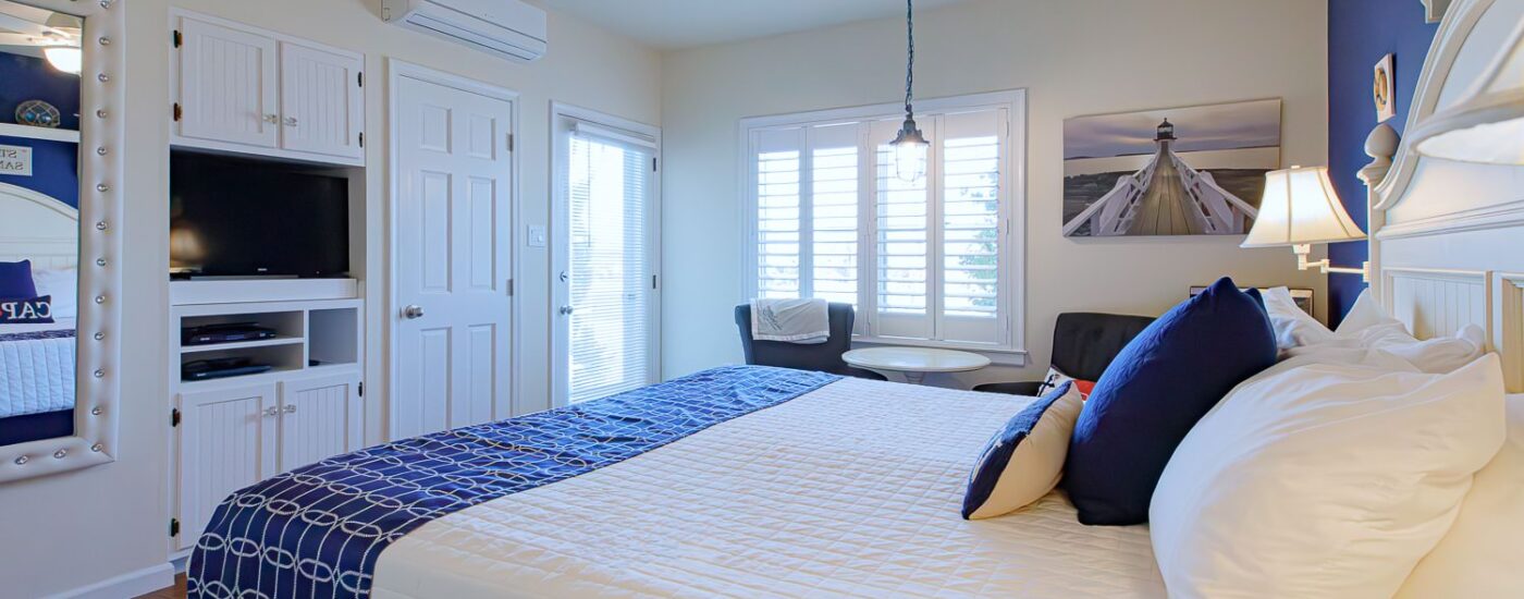 Bedroom with blue and white walls, hardwood flooring, white wood bed, white bedding, and sitting area
