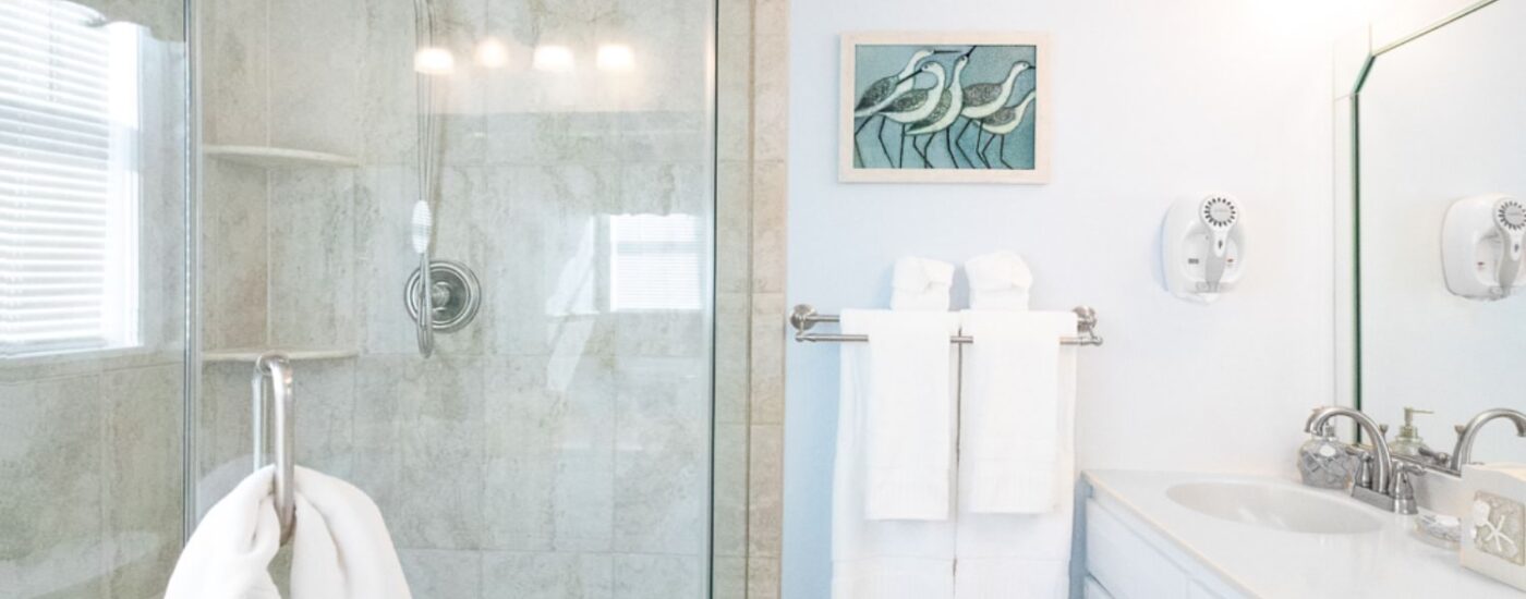 Bathroom with light blue walls, walk in tiled shower, white vanity, and white countertop