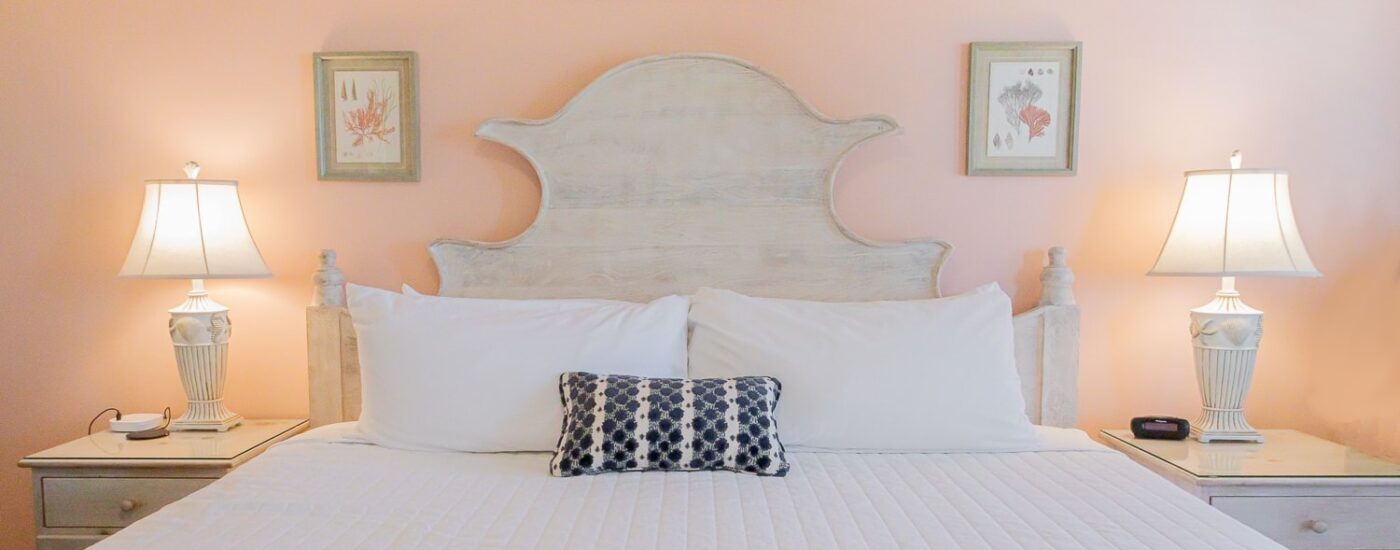 Bedroom with peach walls, wood bed, white bedding, and two nightstands each with a lamp
