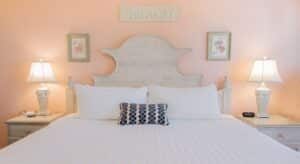 Bedroom with peach walls, wood bed, white bedding, and two nightstands each with a lamp