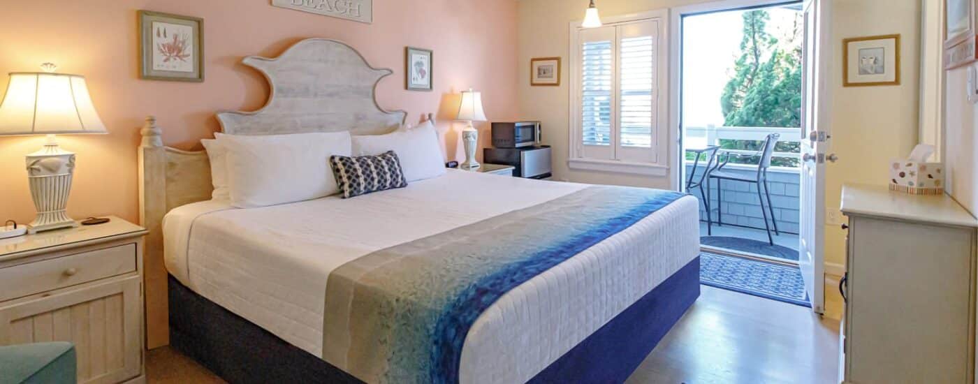 Bedroom with light pink and yellow walls, hardwood flooring, wood bed, white bedding, and open door to balcony