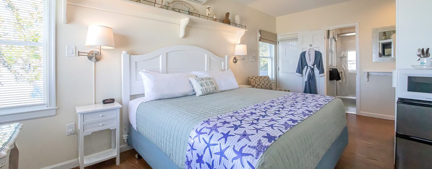 Bedroom with light cream walls, hardwood flooring, white wood bed, light green and white bedding, mini fridge, and microwave