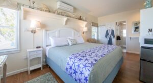 Bedroom with light cream walls, hardwood flooring, white wood bed, light green and white bedding, mini fridge, and microwave