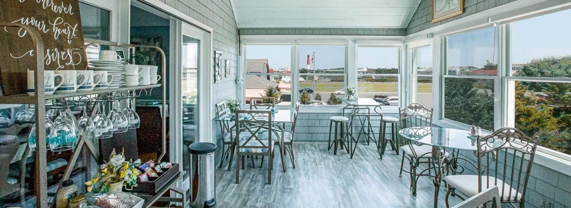 Large breakfast dining area with multiple windows, hardwood flooring, and metal chairs and tables with glass tops