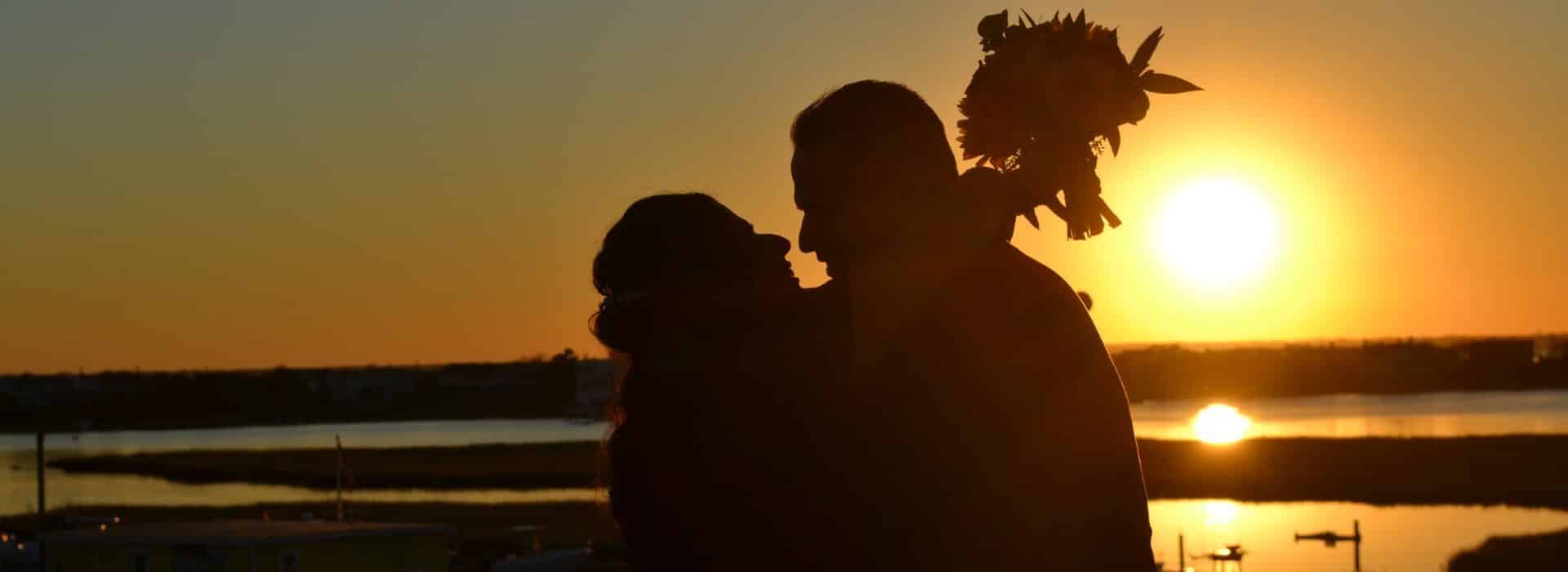 Woman holding a bouquet of flowers hugging a man with the setting sun in the background