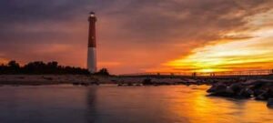 View of water at sunset with red and white lighthouse in the background