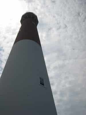 Lighthouse upclose, from below. Light coming on it through clouds.