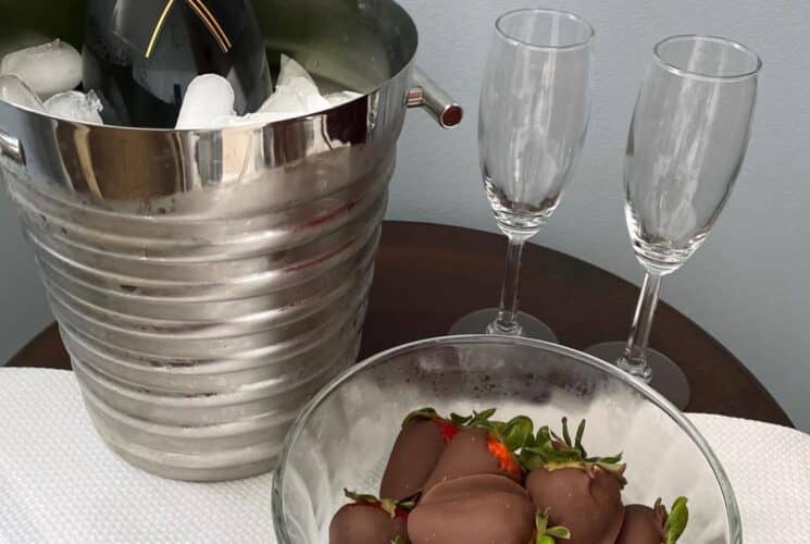 Silver bucket chilling wine next to a chilled bowl full of chocolate covered strawberries and two Champagne flutes