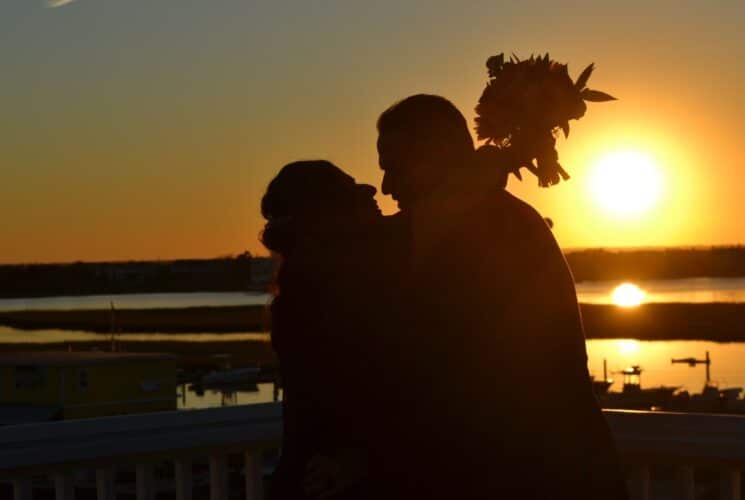 Woman holding a bouquet of flowers hugging a man with the setting sun in the background