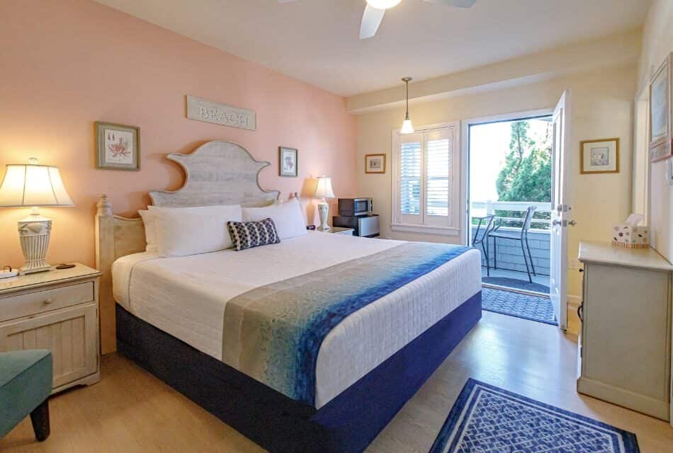Bedroom with light pink and yellow walls, hardwood flooring, wood bed, white bedding, and open door to balcony