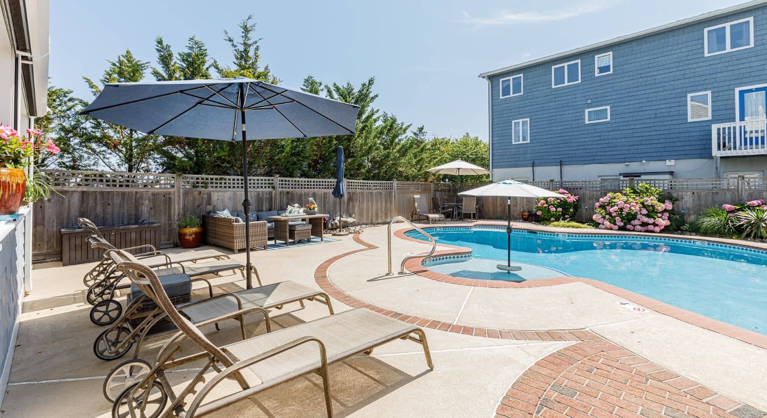 Exterior view of property with light gray shake siding and white trim, patio, pool, and patio furniture