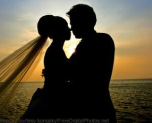 Silhouette of couple about to kiss (bride and groom). Veil blowing behind her (left side). Sunset. 