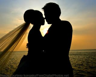 Silhouette of couple about to kiss (bride and groom). Veil blowing behind her (left side). Sunset.